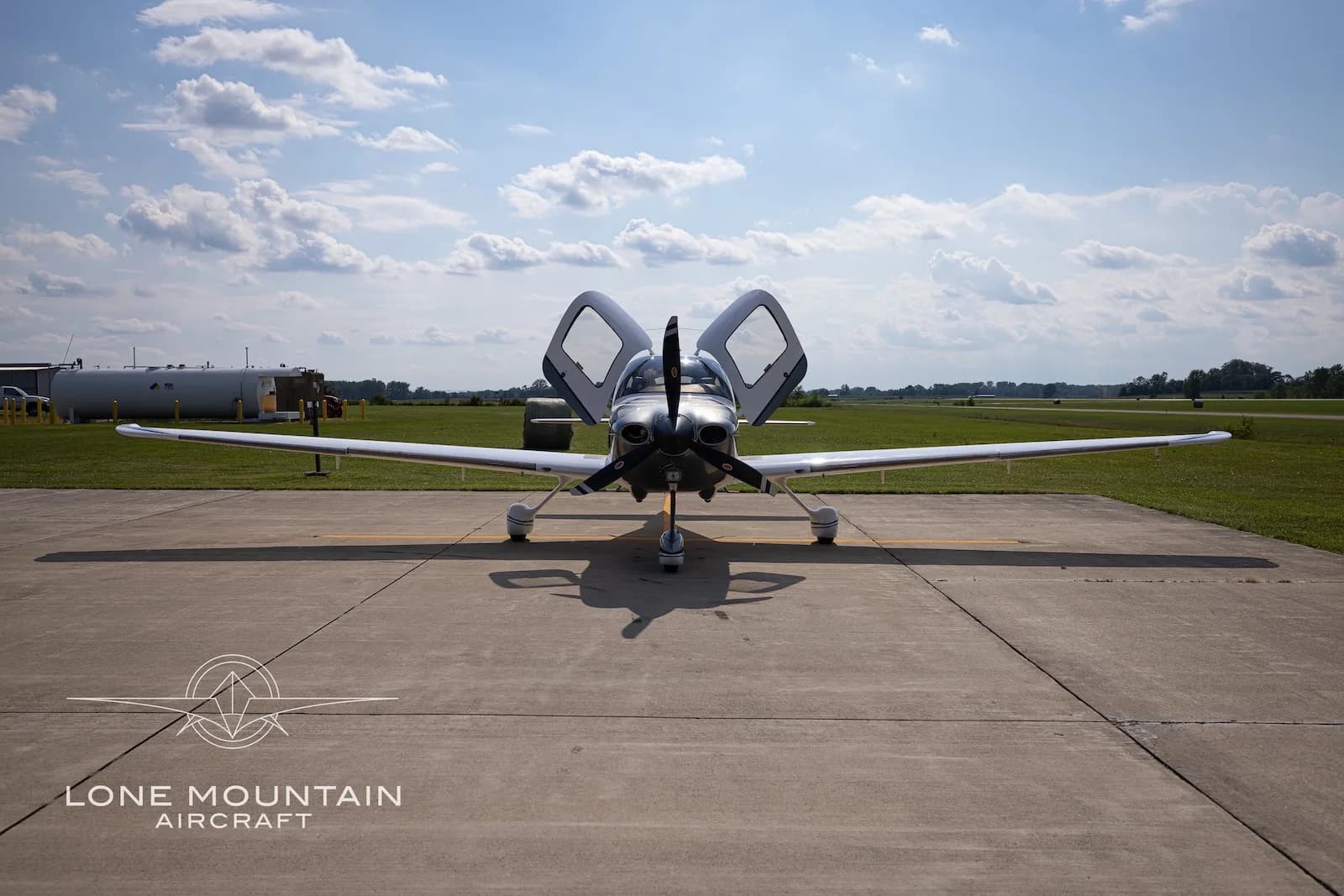 A head-on view of the white and silver Cirrus SR22 aircraft N92BZ with blue accents, parked on an airfield with its doors open.