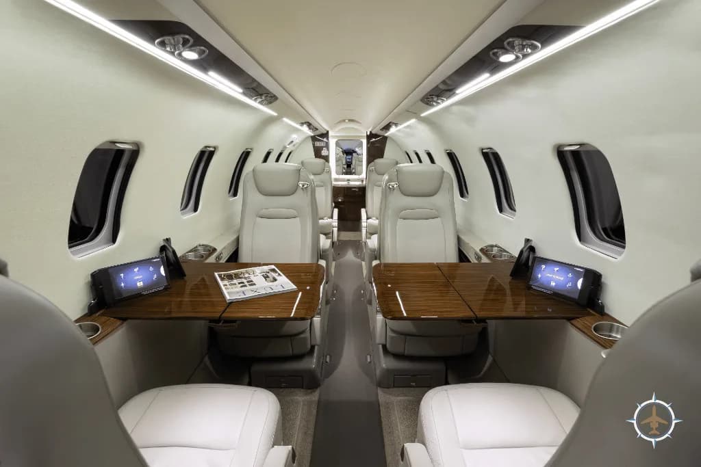 The luxurious cabin interior of a business jet with light-colored leather seats and wooden tables.