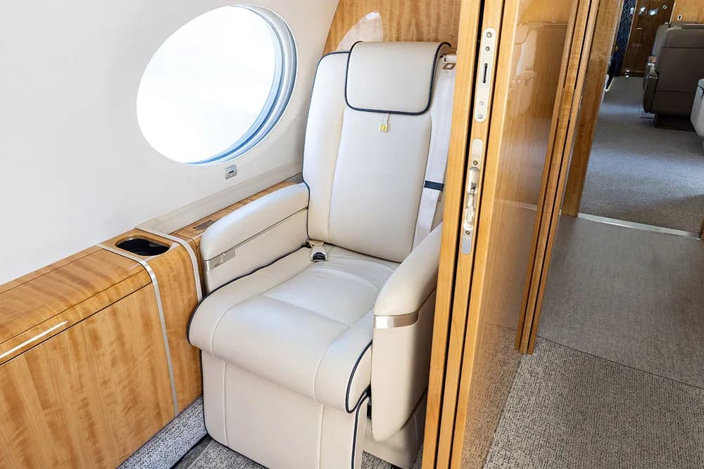A view down the aircraft cabin aisle from the galley, showing light wood paneling and cream seats.