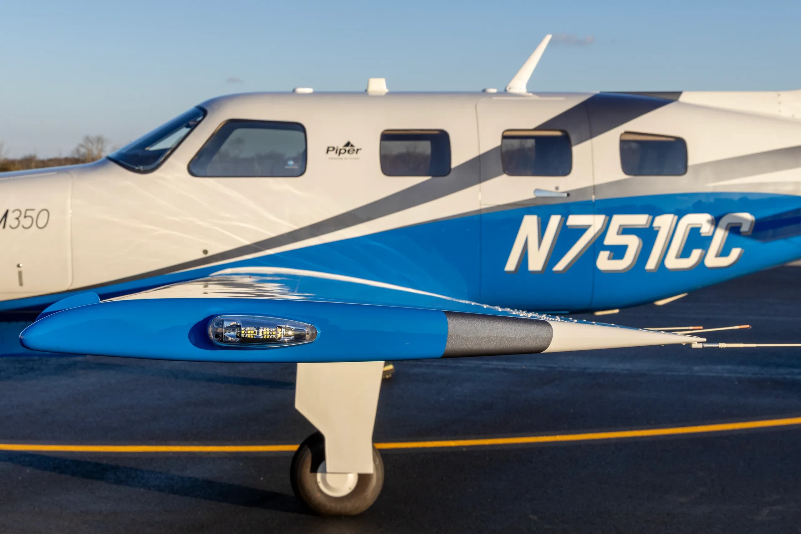 A close-up view of the wingtip and fuselage of a Piper M350 aircraft, registration N751CC, showing the blue and white paint.