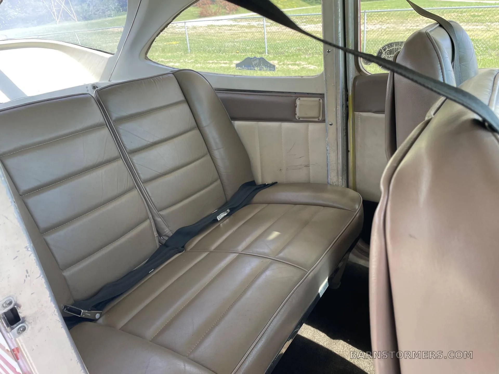 The tan rear bench seat of a Cessna aircraft cabin with a seatbelt across it.