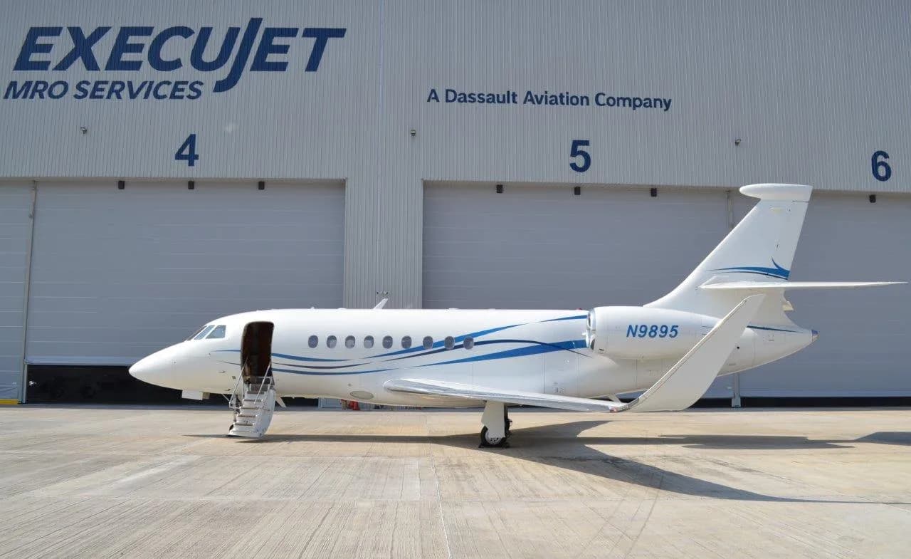 A white business jet with blue swooping lines is parked on a tarmac in front of an ExecuJet MRO Services hangar.