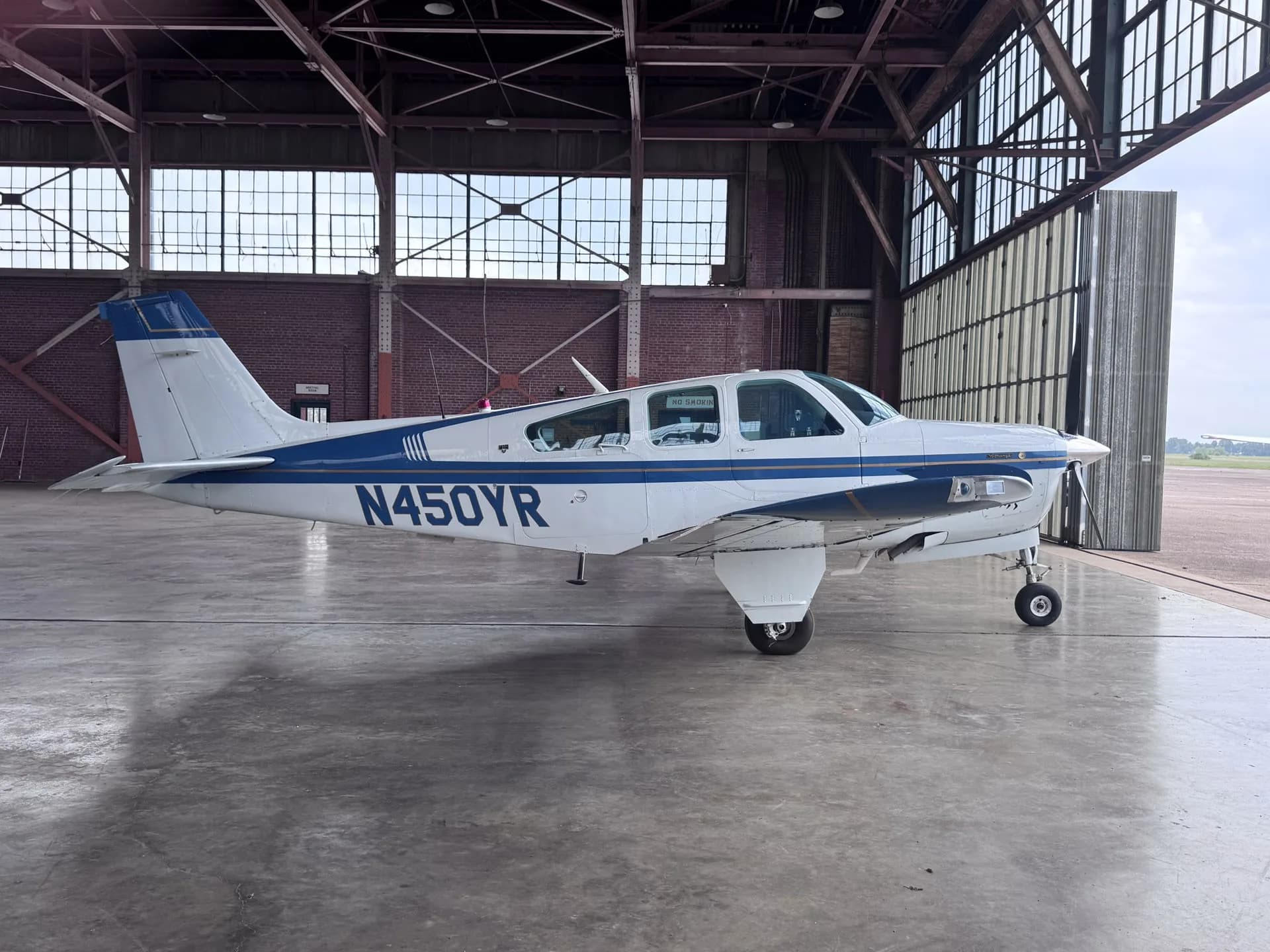 A white and blue Beechcraft Bonanza F33A aircraft with registration N450YR parked in a hangar.