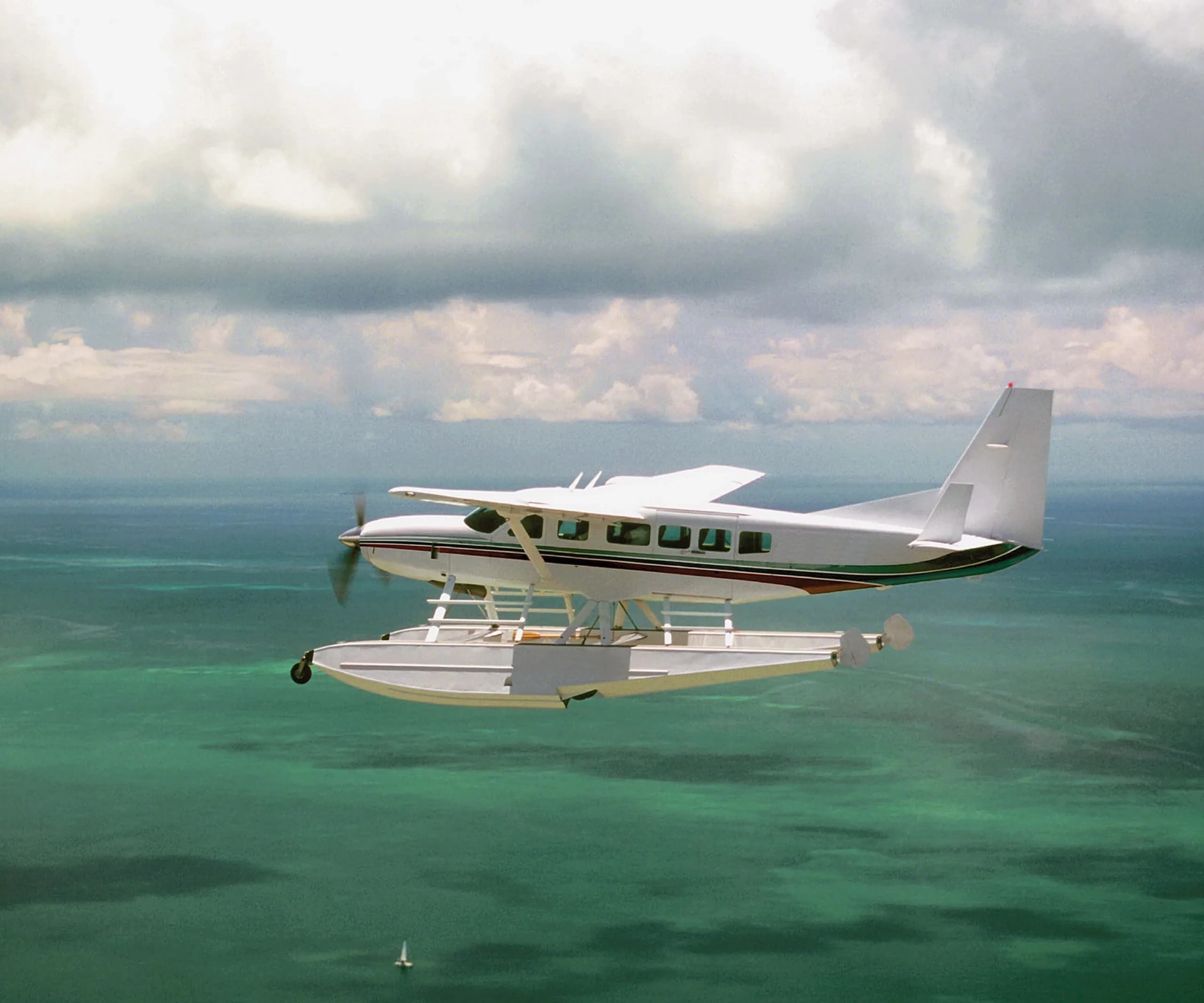 A white and red Cessna Caravan seaplane flies over the ocean.