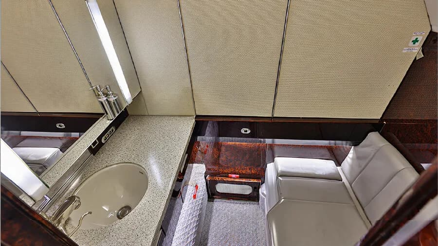 The lavatory of a business jet with a sink, mirror, and light-colored seating.