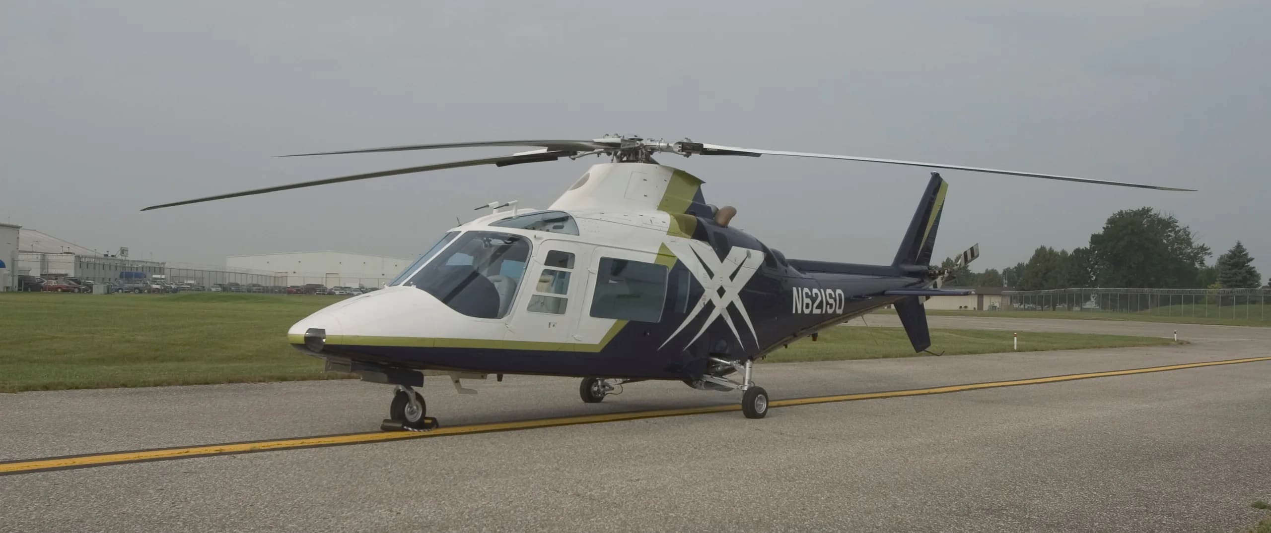 A white and dark blue helicopter with a green stripe and N621SD tail number parked on an airfield.