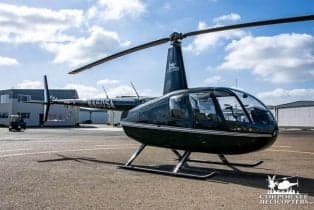 Robinson R44 helicopter on the tarmac with a dark green paint scheme.