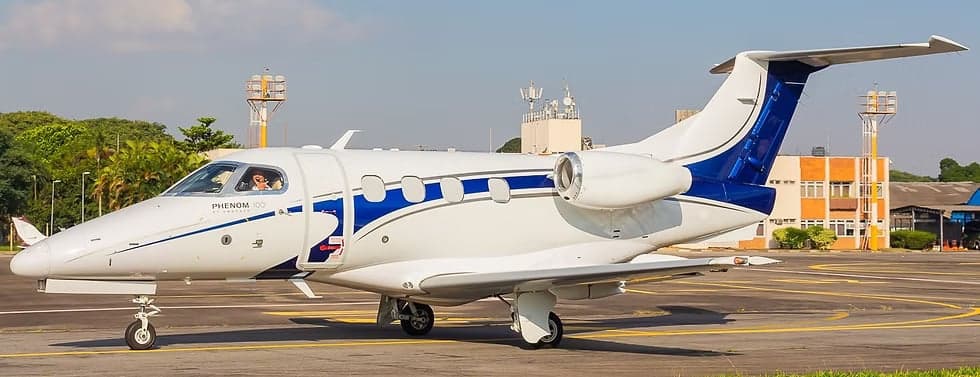 A Phenom 300E aircraft is parked on the tarmac with a blue and white paint scheme.