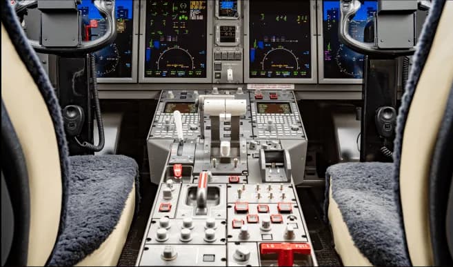 The cockpit of a modern private jet displays multiple digital screens, control yokes, and a central throttle quadrant.