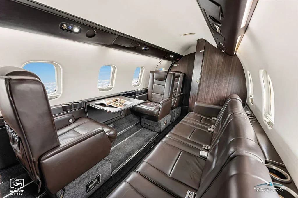 The luxurious interior cabin of a business jet featuring brown leather seats and dark wood paneling.