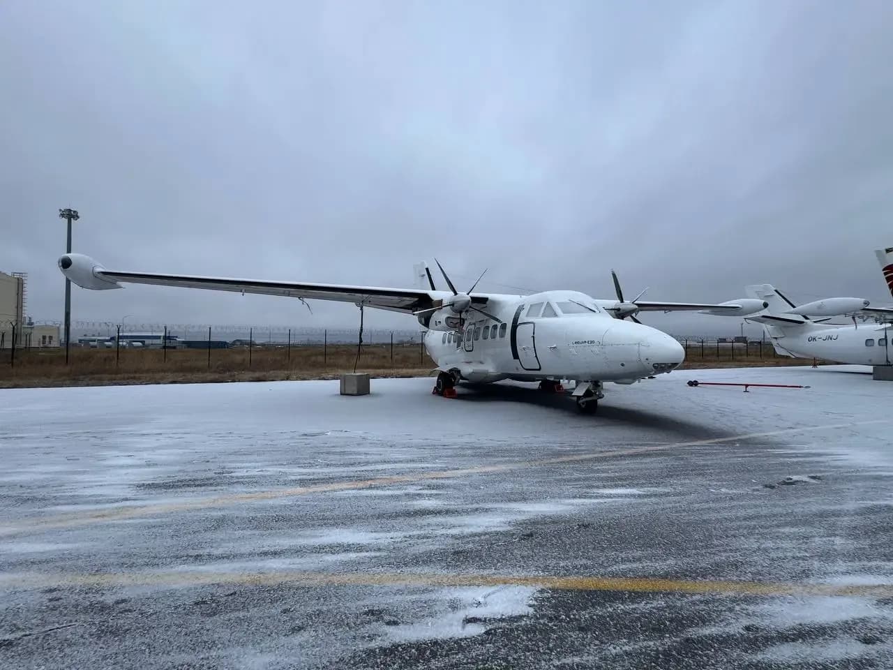 A white Let L-410 Turbolet twin-engine turboprop aircraft is parked on a snowy tarmac under an overcast sky.