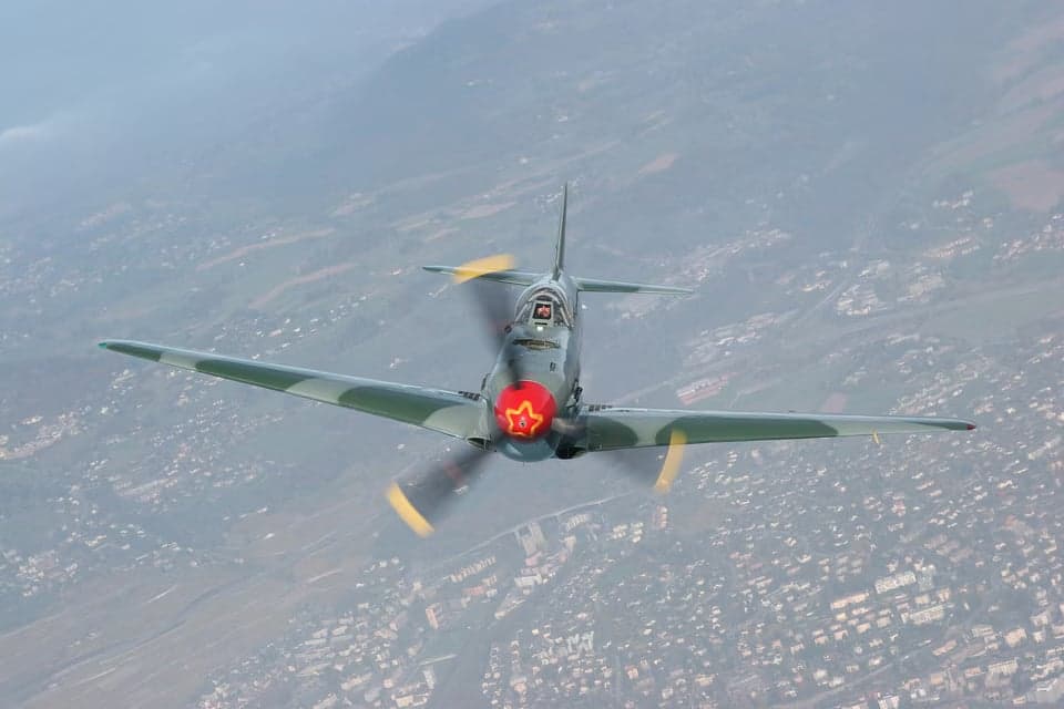 Yak-3 in flight over a mountainous landscape.