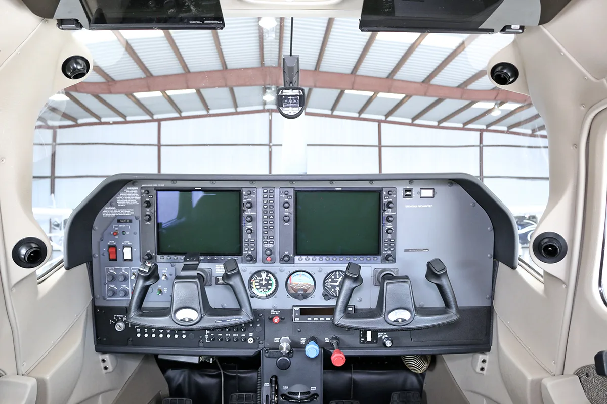The cockpit of an aircraft, featuring a modern glass panel with two large displays and dual yokes.