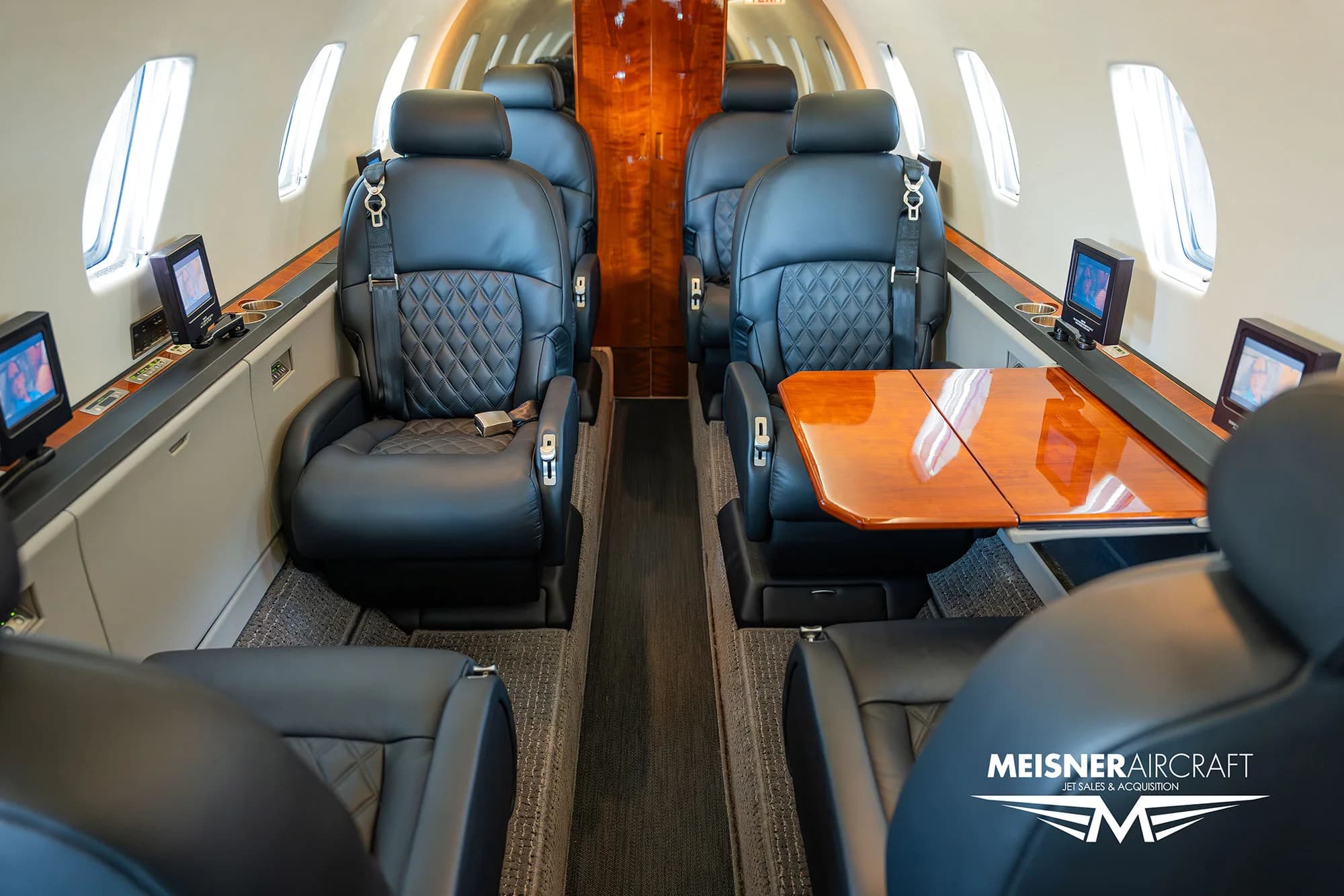 The luxurious interior cabin of a Citation Excel business jet with black leather seats and a polished wooden table.