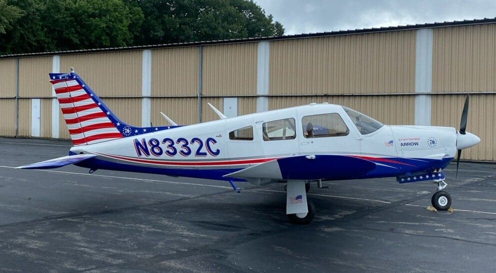 Side view of a white and blue Piper PA-28 with registration N8332C parked on the tarmac.