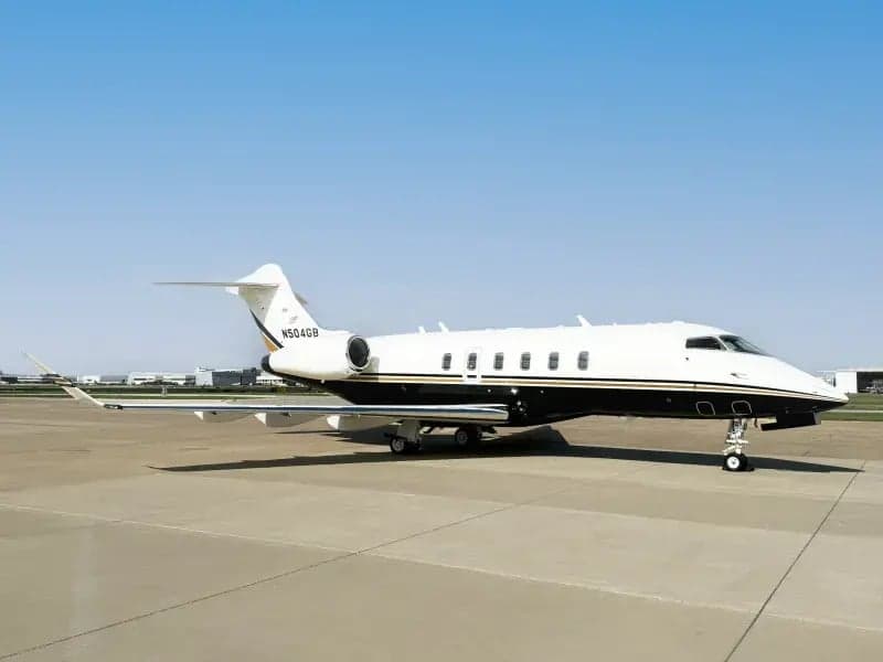 Side view of a Challenger 300 aircraft with a white and black paint scheme on the tarmac.