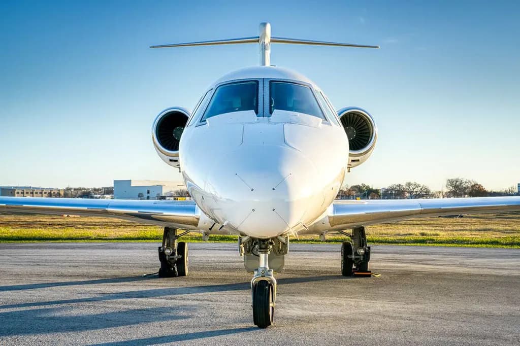 A white business jet (N24KT) is viewed head-on, parked on a tarmac under a clear blue sky.