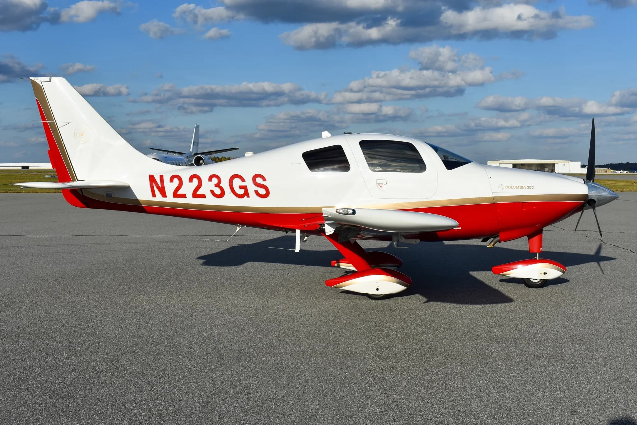 Side view of a white and red Columbia 350 aircraft with tail number N223GS, parked on an airfield.