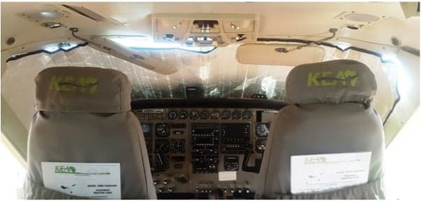 The aircraft's front cabin seats, covered in grey fabric with "KEAP" logos, face the cockpit.