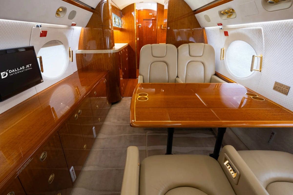 Gulfstream G450 cabin interior with a wooden table and beige leather seats.