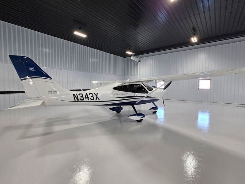 A white and blue Tecnam P2008 Light Sport aircraft (N343X) is parked in a hangar, viewed from the front-right.