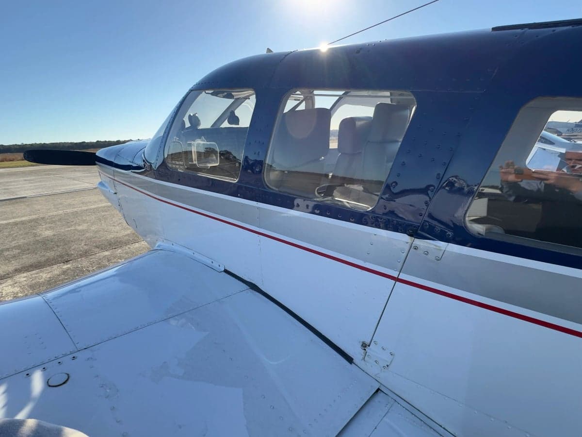 Close-up of the cabin windows of a blue and white Piper Cherokee aircraft.