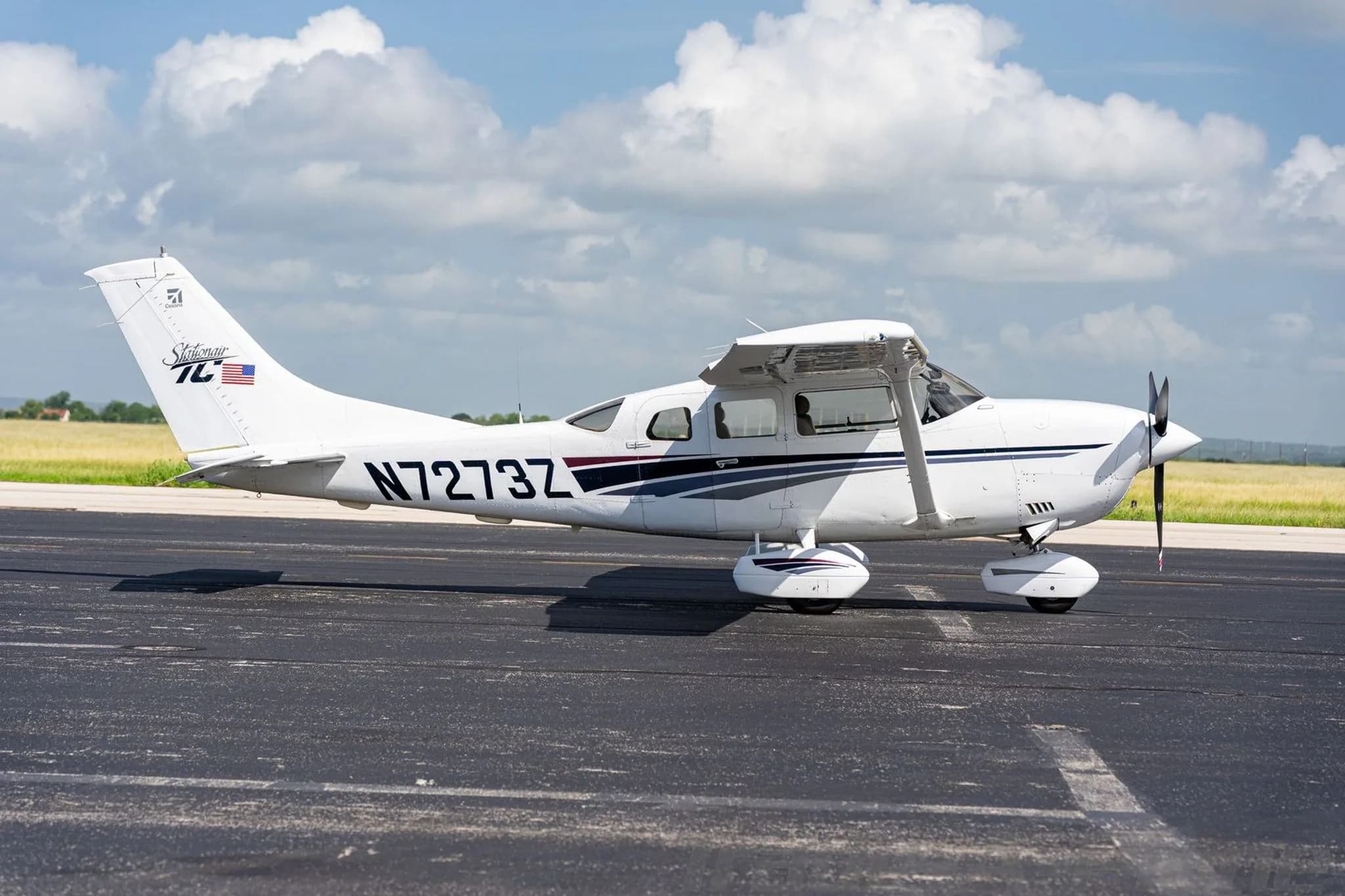 A side view of a white Cessna Stationair TC with dark blue and gray stripes on a tarmac.