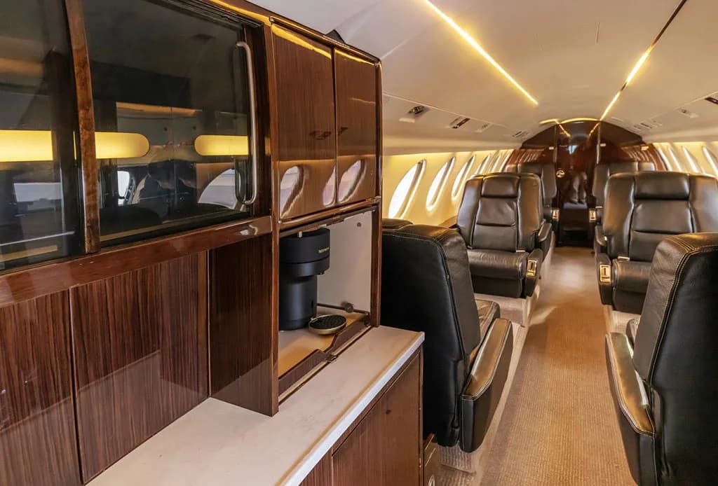 A view of the aircraft's galley area with dark wood cabinetry, a Nespresso machine, and black leather seats in the background.