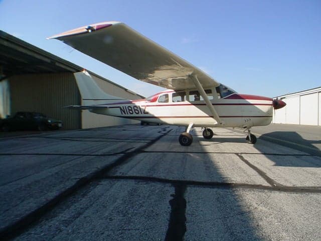 A white and red Cessna 206 aircraft (N1861Z) parked on an asphalt ramp, viewed from the rear-right.