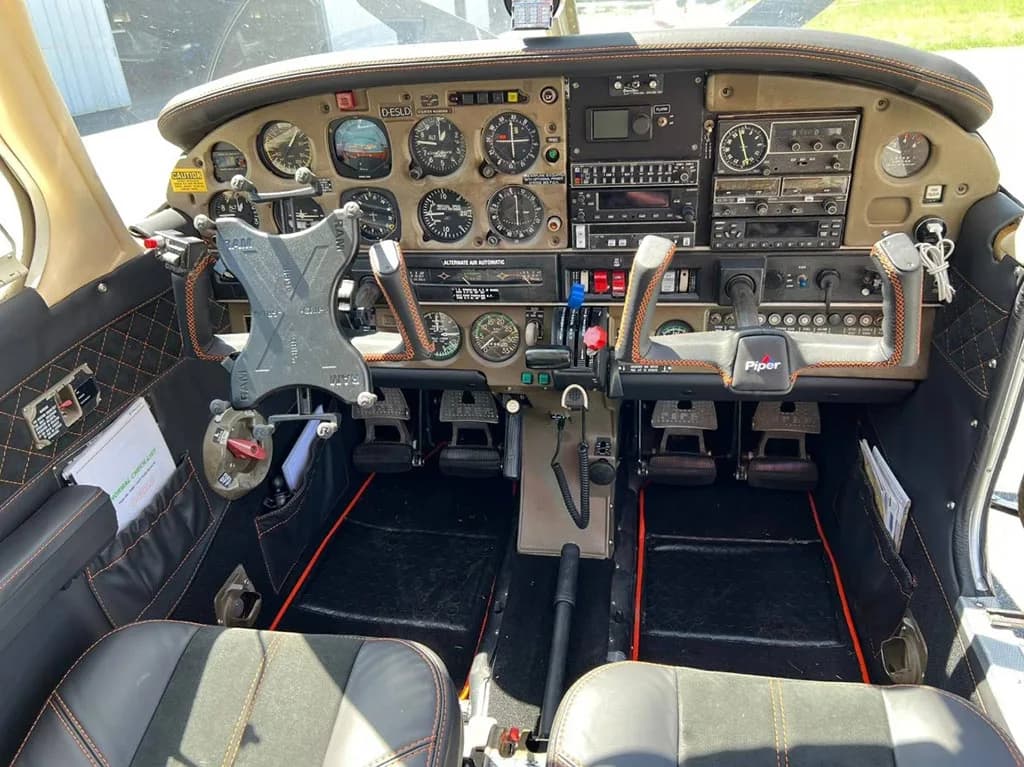 The cockpit of a Piper Arrow III showing the instrument panel, yokes, and pedals.