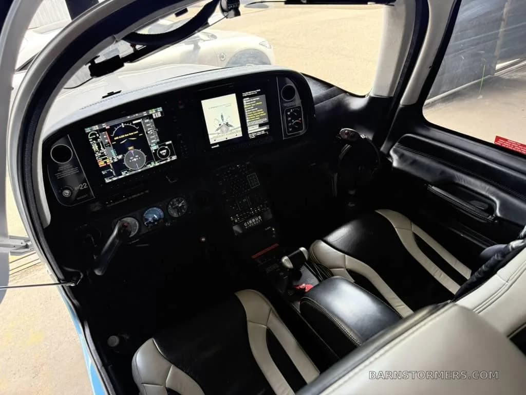 The cockpit of a Cirrus SR22 aircraft, showing the instrument panel with multiple screens and black and white leather seats.