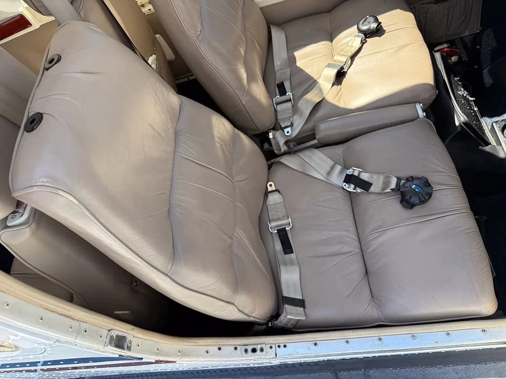 A close-up view of the tan leather seats in the aircraft's cabin, with seatbelts visible.