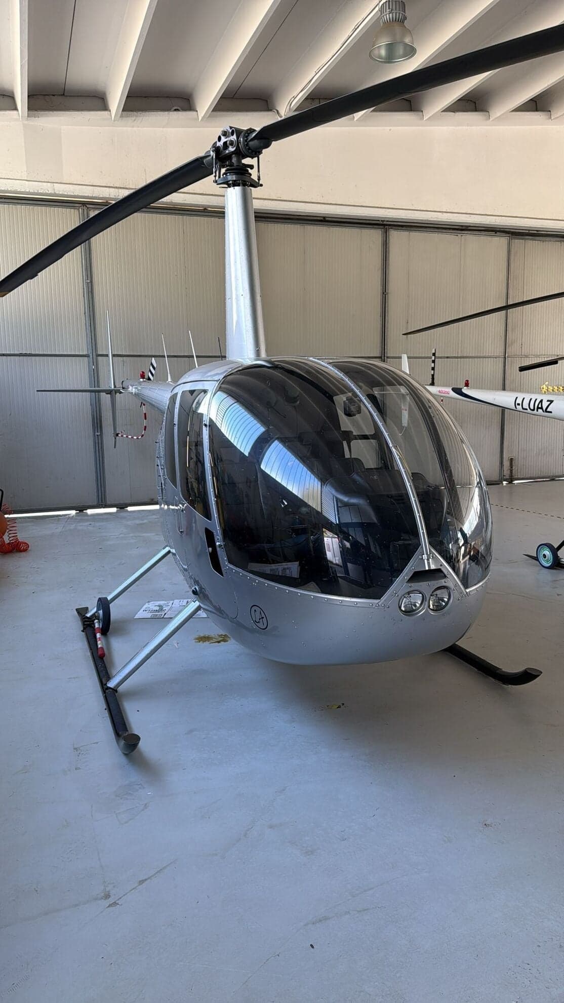 Front view of a silver Robinson R44 helicopter inside a hangar.