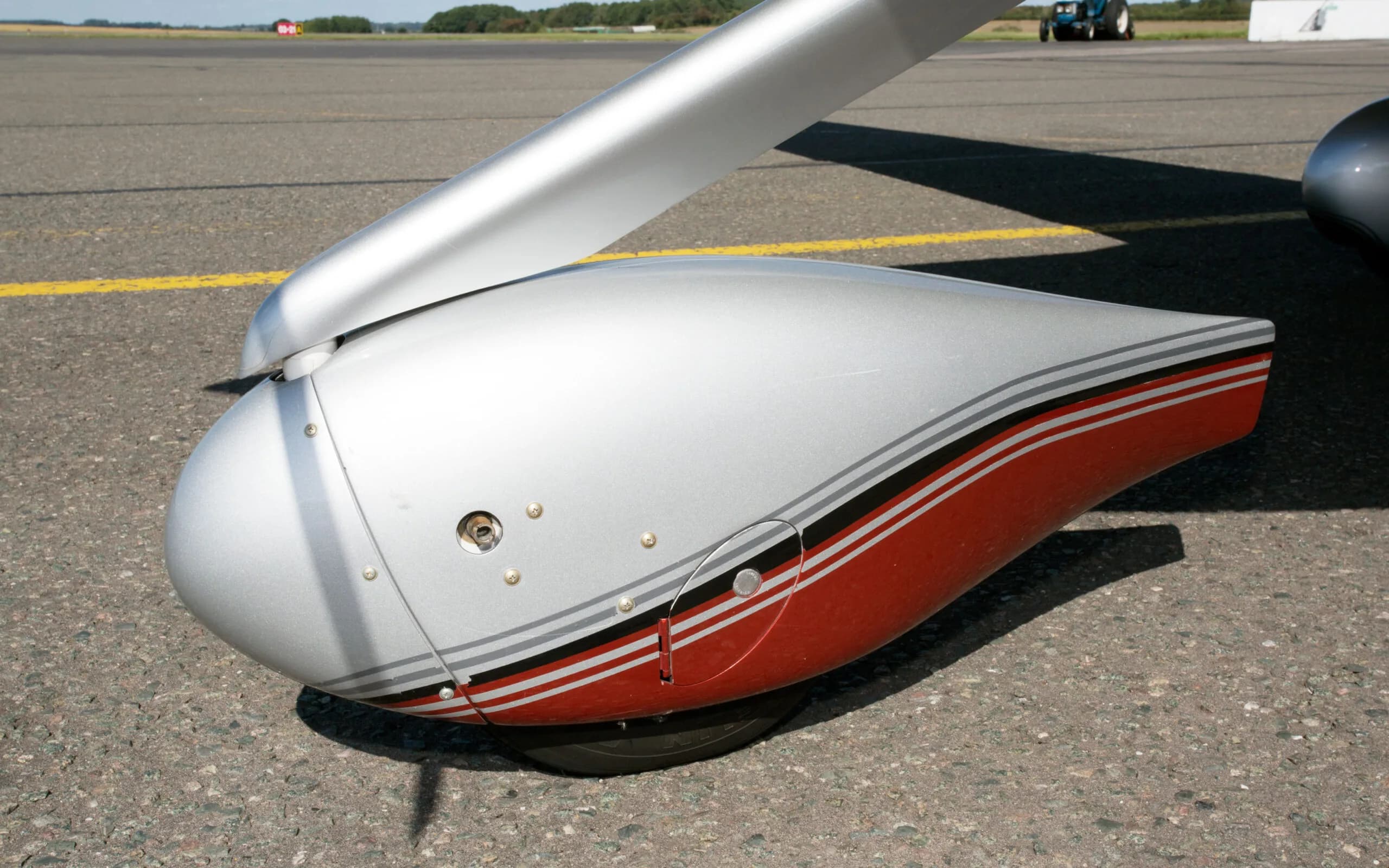 A close-up of the red and silver nose landing gear fairing of a Cirrus SR22T GTS aircraft on an asphalt surface.