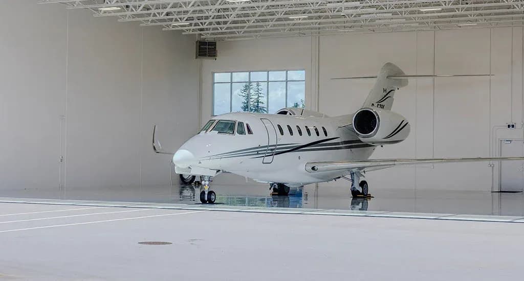 A white business jet, registration C-FJDM, with black and grey stripes, parked in a clean, well-lit hangar.