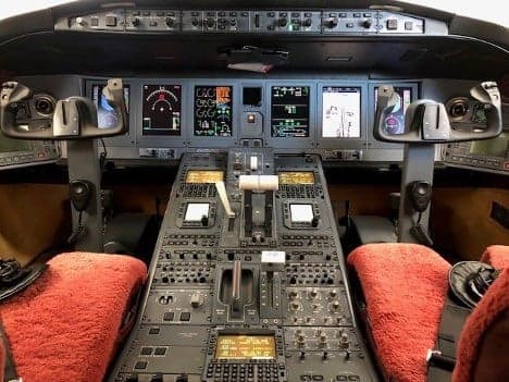 The cockpit of a Bombardier Challenger 604, showing the instrument panel, yokes, and center console with red sheepskin seat covers.