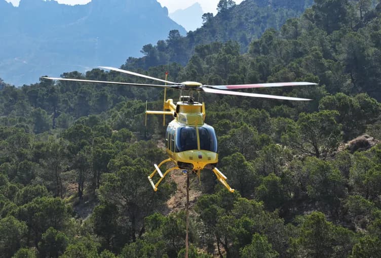 Yellow helicopter flying over a forest.