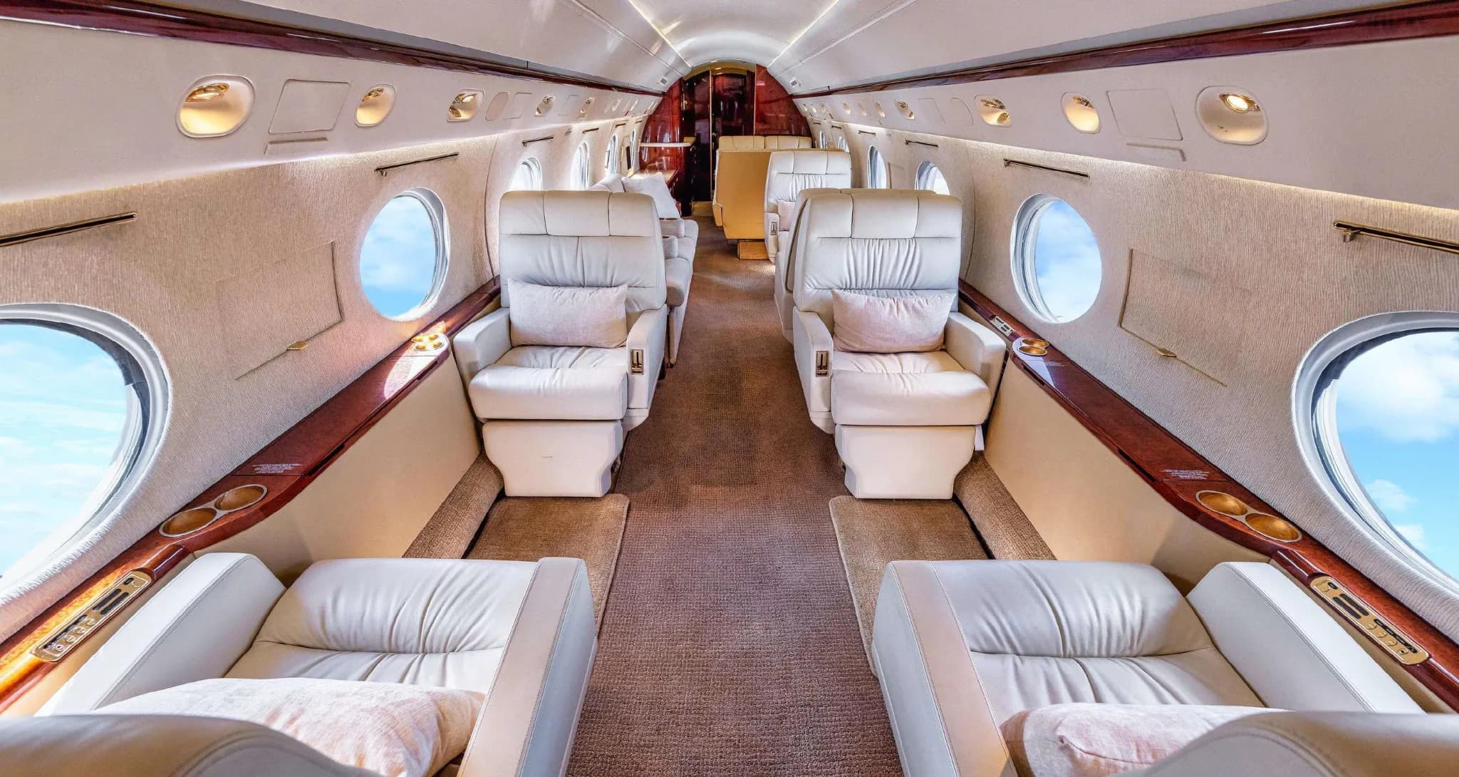 The luxurious cabin interior of a Gulfstream G550, featuring cream leather seats and large windows.