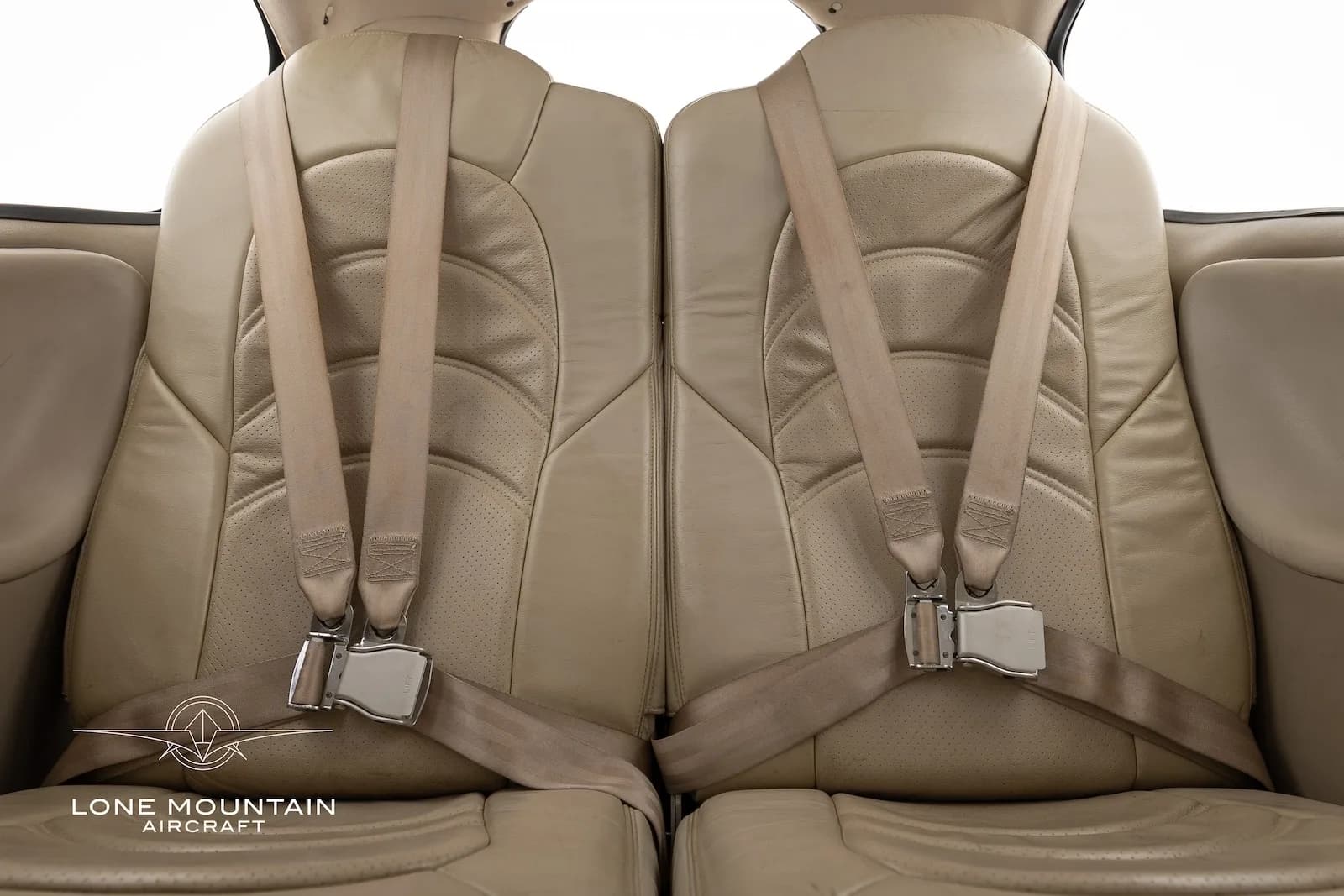 Close-up view of the beige leather front seats of a Cirrus SR22 aircraft cabin, showing seatbelts and buckles.