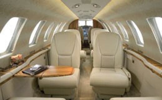 The interior of a jet with cream-colored leather seats and wood trim.