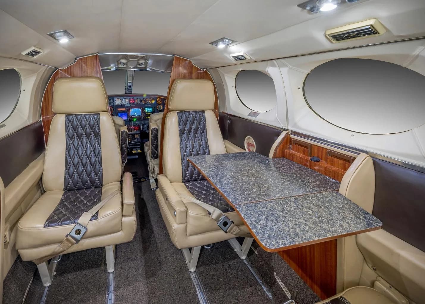 The aircraft cabin interior with beige and black quilted seats and an extended table.