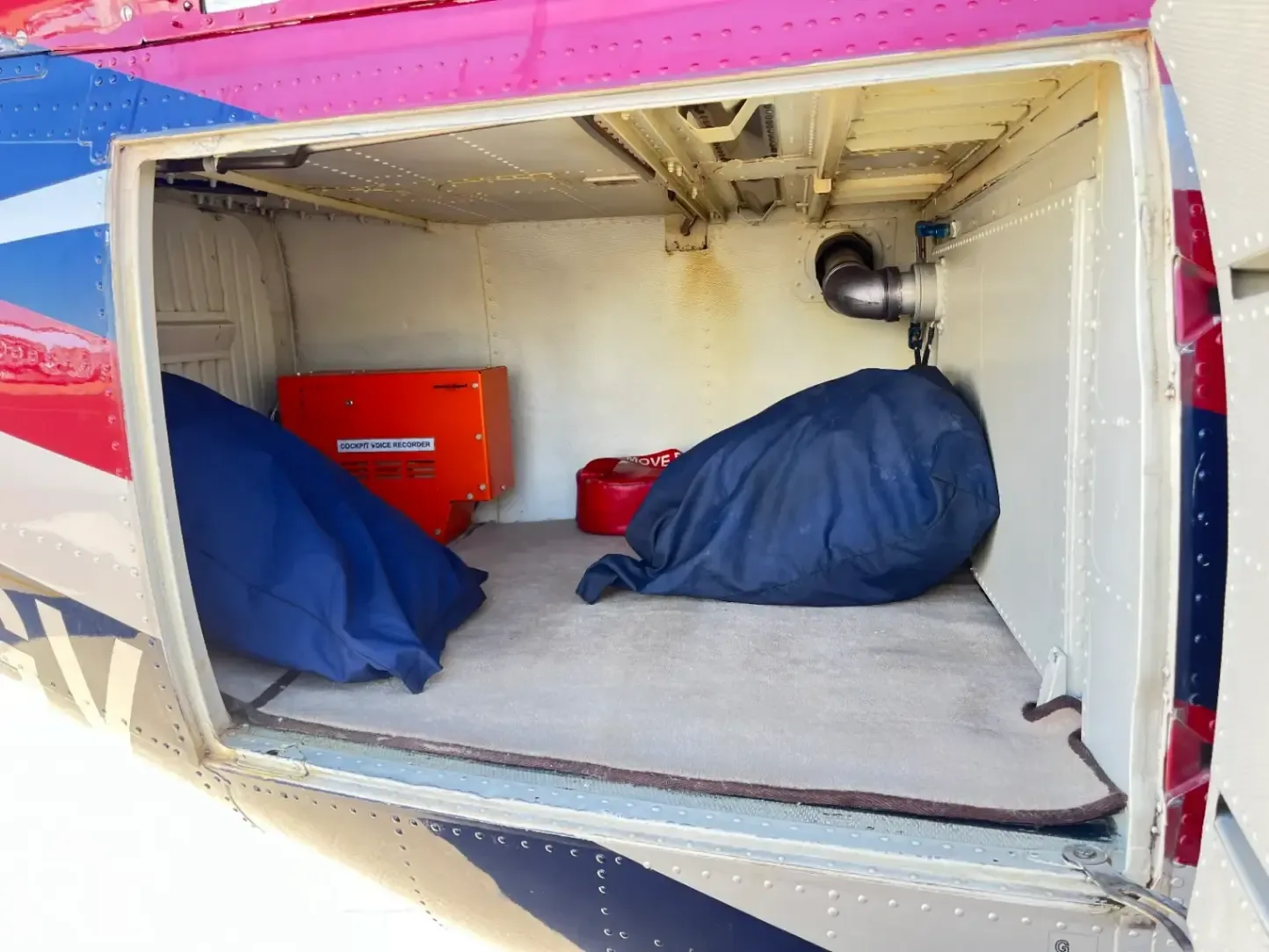 The open cargo compartment of the helicopter shows storage bags and a cockpit voice recorder.
