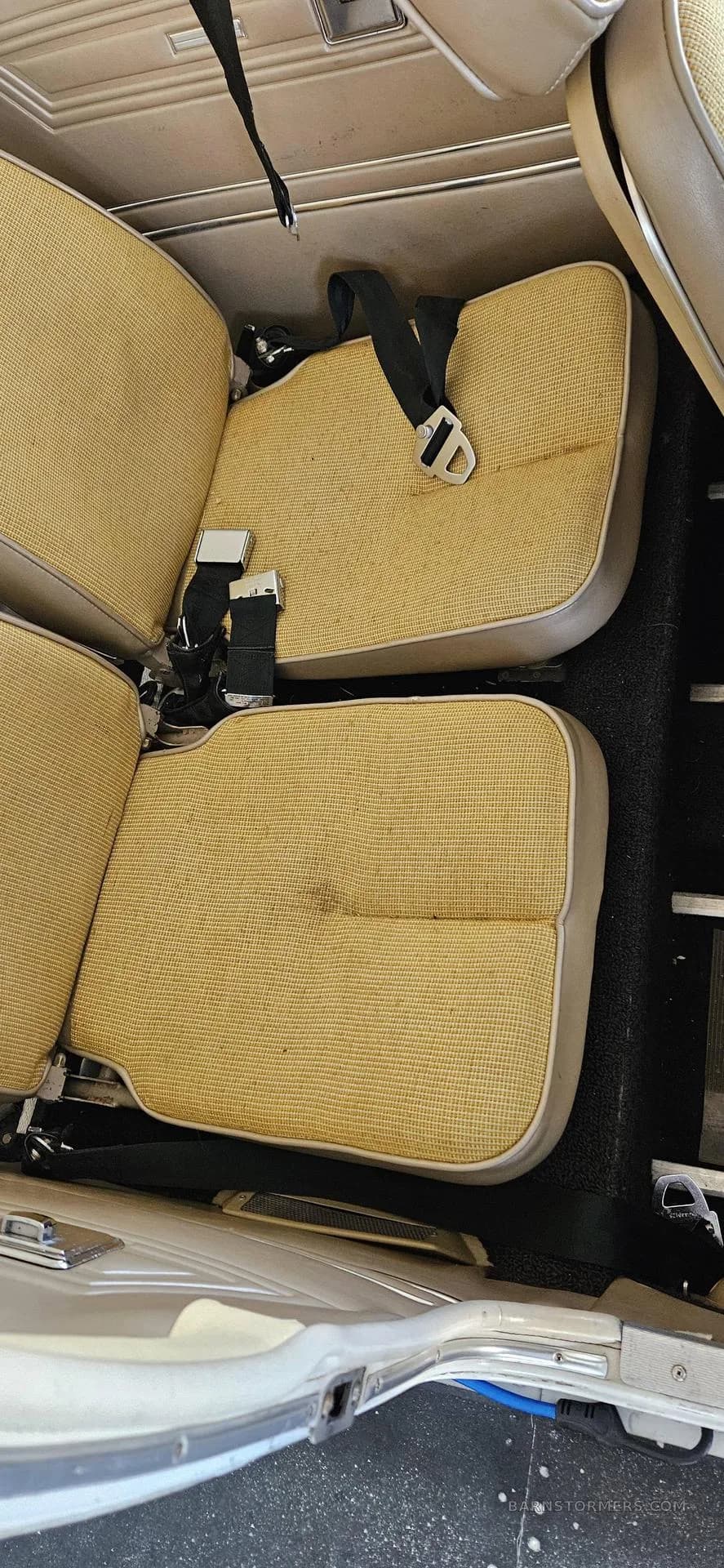 Two tan fabric rear seats with black seatbelts in the cabin of a light aircraft.