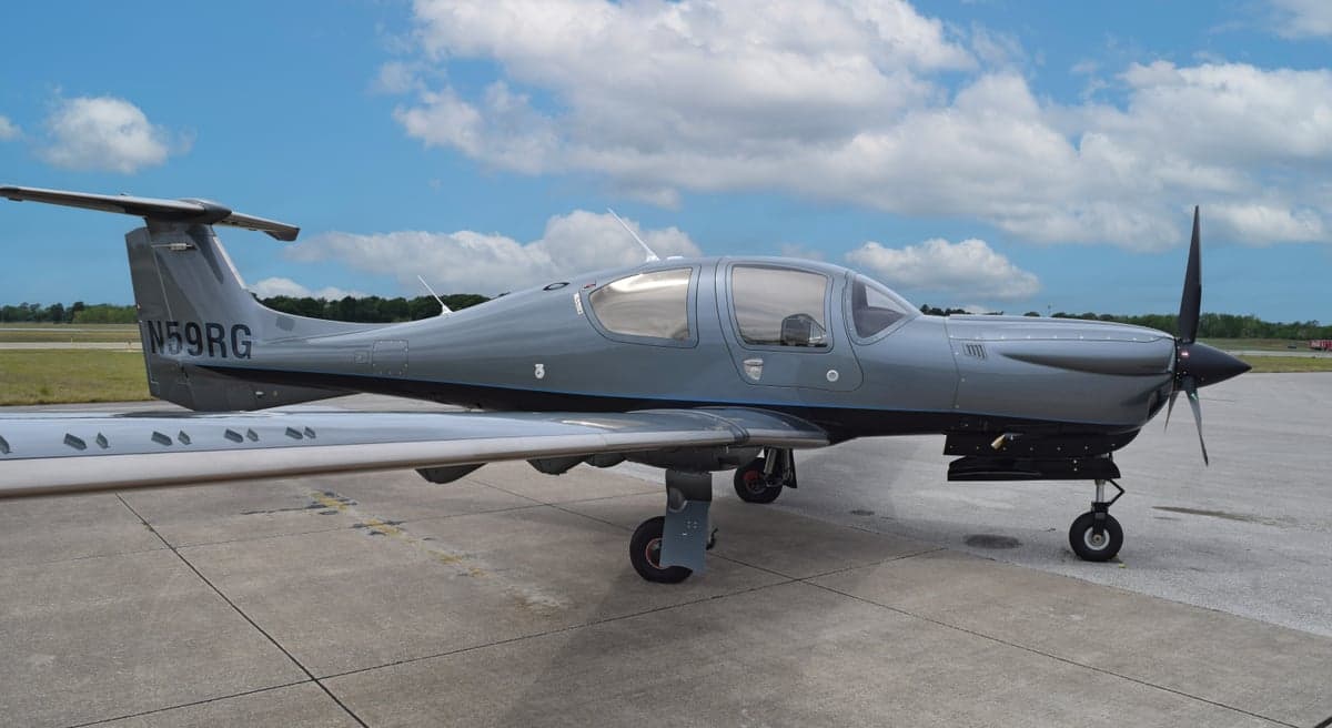 A gray Diamond DA50 RG aircraft, registration N59RG, with blue accents, parked on an airfield under a partly cloudy sky.