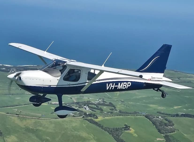A Glasair Sportsman aircraft in flight over a green landscape.