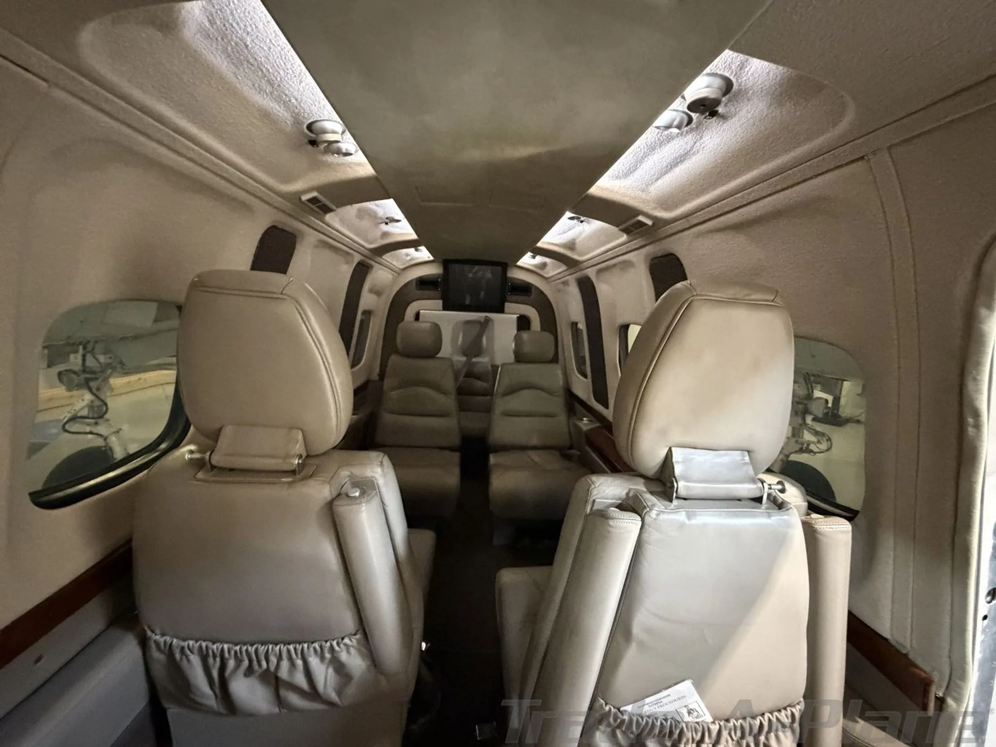 The aircraft cabin interior with beige leather seats facing forward, viewed from the rear.