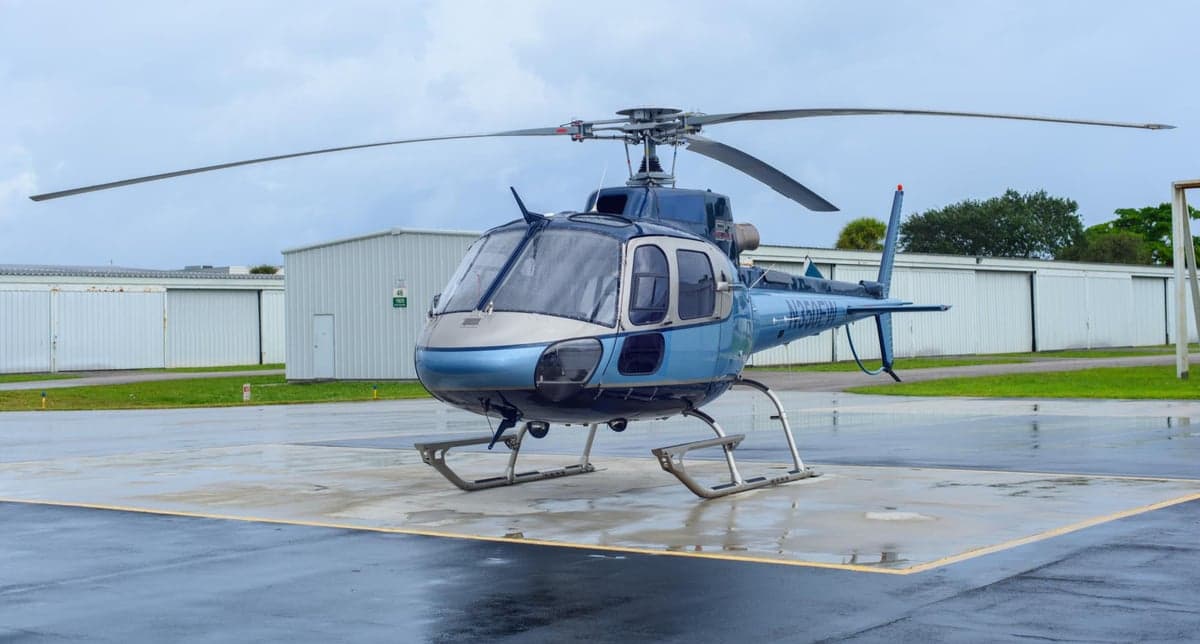 A Eurocopter AS350B3 Ecureuil helicopter is parked on a wet tarmac.