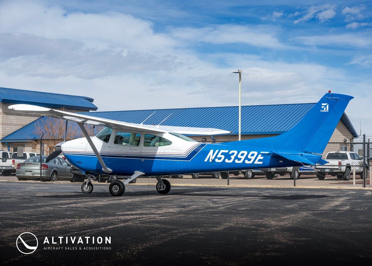 A Cessna aircraft with a blue and white paint scheme parked in front of a hangar.