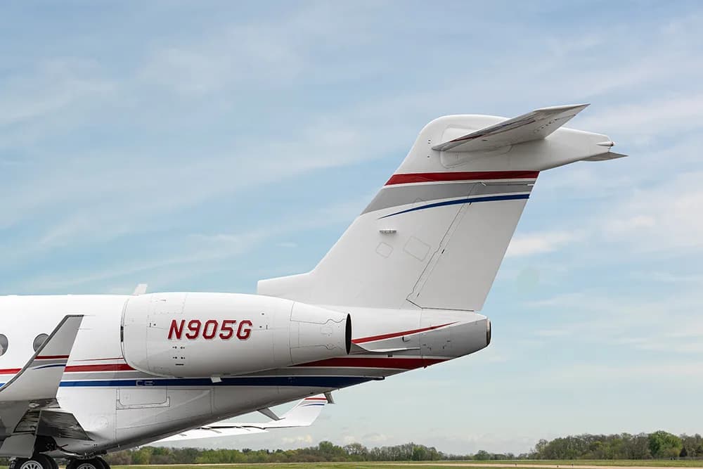 A close-up of the tail and rear fuselage of a white business jet, showing the registration N905G and red and blue stripes.