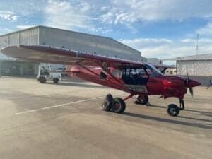 Side view of a red Cubcrafters aircraft parked on the tarmac.